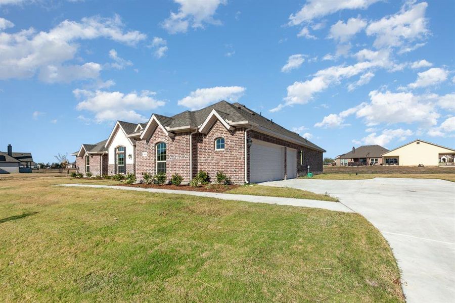 View of front of property with brick siding, a front yard, driveway, and roof with shingles