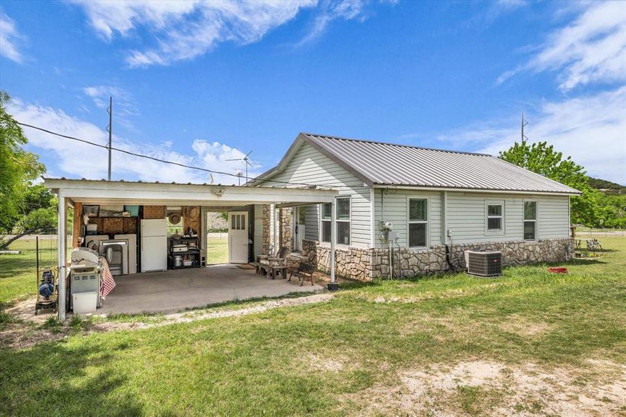 Rear view of property featuring stone siding, a yard, a patio area, and a metal roof