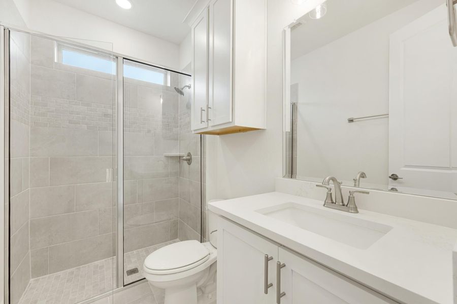 Bathroom with glass-enclosed tile shower, white vanity with quartz countertop, and toilet