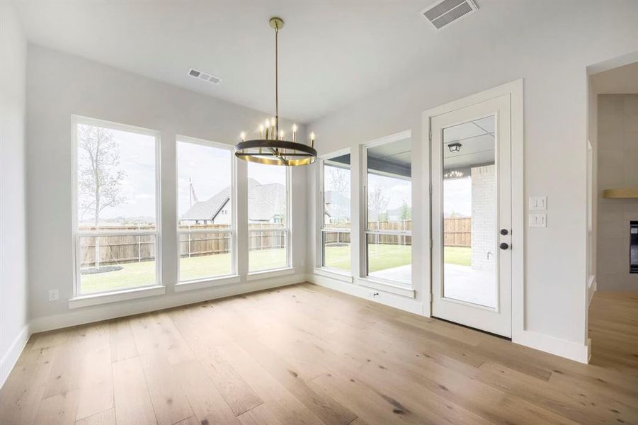 Bright interior with wood-finish flooring, a contemporary chandelier, multiple large windows, a glass-paneled exterior door, and white baseboards