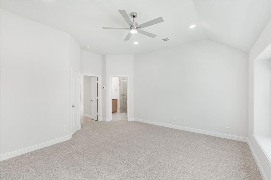 Empty bedroom with vaulted ceiling, ceiling fan, carpet flooring, and ensuite bathroom doorway visible Empty bedroom with vaulted ceiling, ceiling fan, carpet flooring, and ensuite bathroom doorway visible