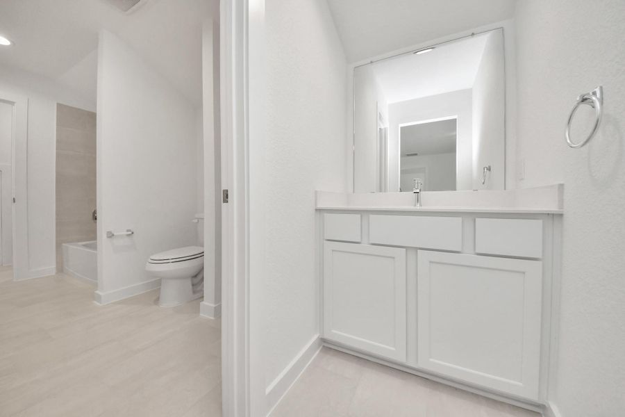 Experience convenience in the secondary bathroom, designed for Jack and Jill arrangements, now with a separate vanity area. This well-appointed space showcases stylish tile flooring, a bath/shower combo with an elegant tile surround, and light-stained wood cabinets. The beautiful light countertop adds a touch of sophistication, combining functionality and aesthetics seamlessly.