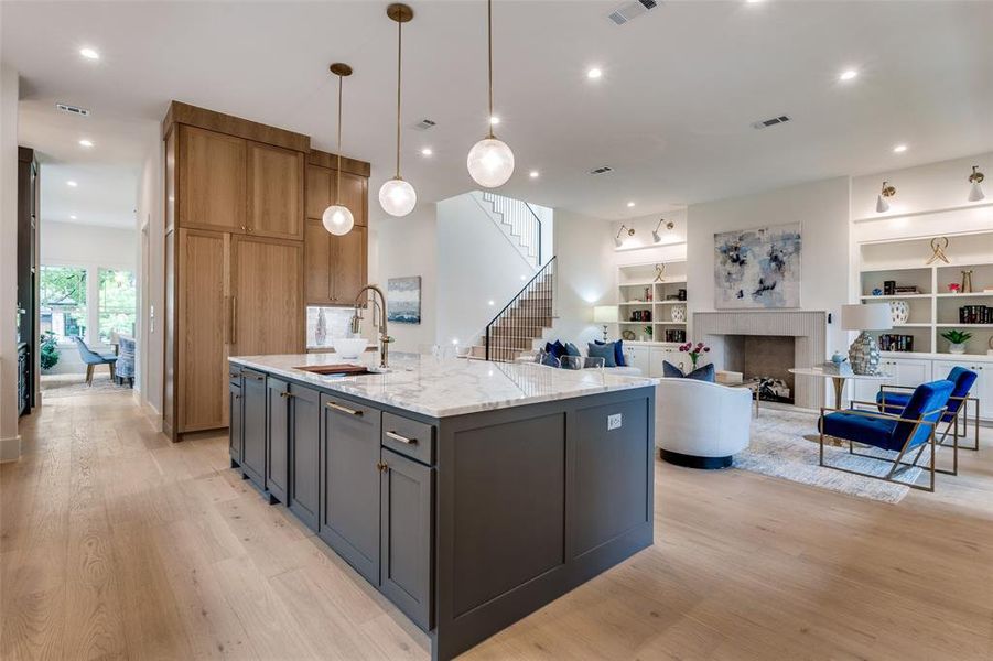 Kitchen featuring light stone countertops, a kitchen island with sink, light wood-type flooring, and a sink Kitchen featuring light stone countertops, a kitchen island with sink, light wood-type flooring, and a sink