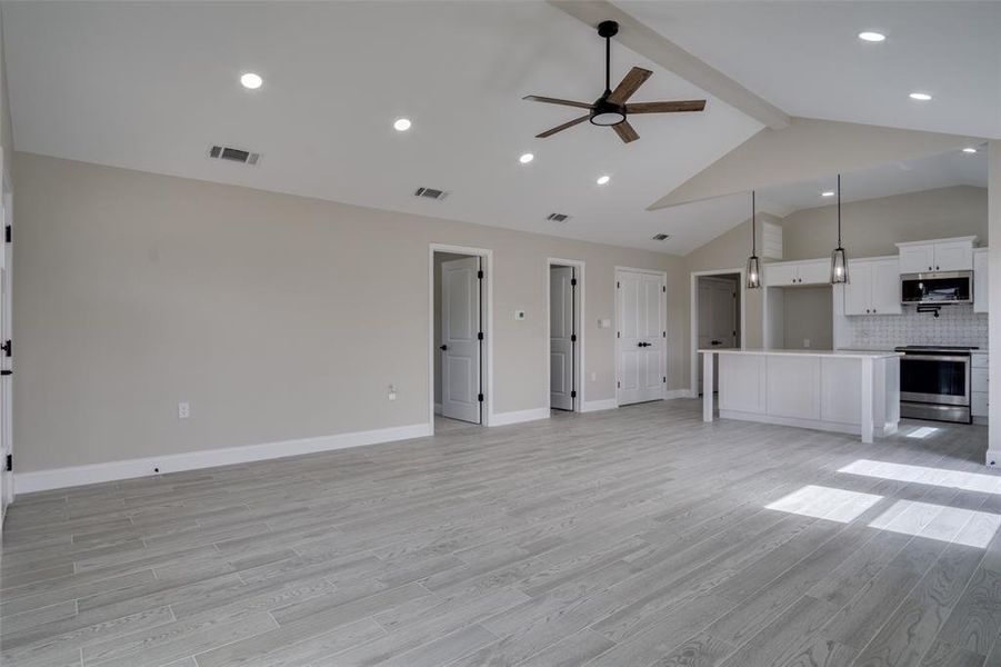 Unfurnished living room with light wood-type flooring, visible vents, beam ceiling, baseboards, and ceiling fan