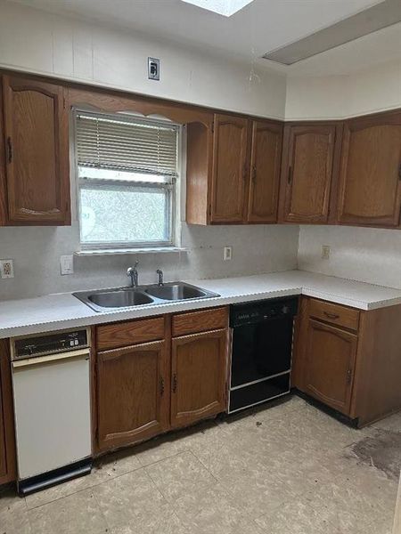 Kitchen with light countertops, dishwasher, and a skylight