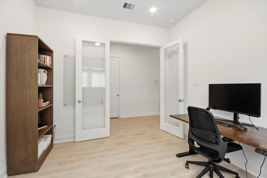 Spacious home office featuring a sleek desk with a modern chair, built-in shelving for storage, and elegant double glass doors for a touch of sophistication.