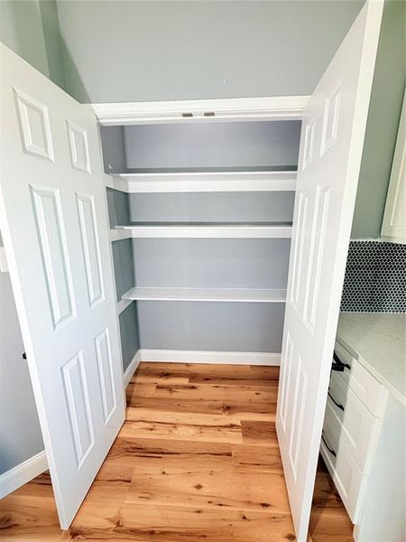 Spacious pantry with multiple shelving units, wood-finish flooring, and crisp white bi-fold doors