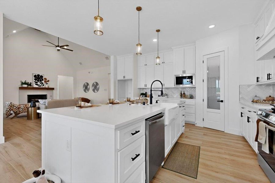 Kitchen featuring white cabinets, vaulted ceiling, open floor plan, light wood finished floors, and decorative light fixtures Kitchen featuring white cabinets, vaulted ceiling, open floor plan, light wood finished floors, and decorative light fixtures
