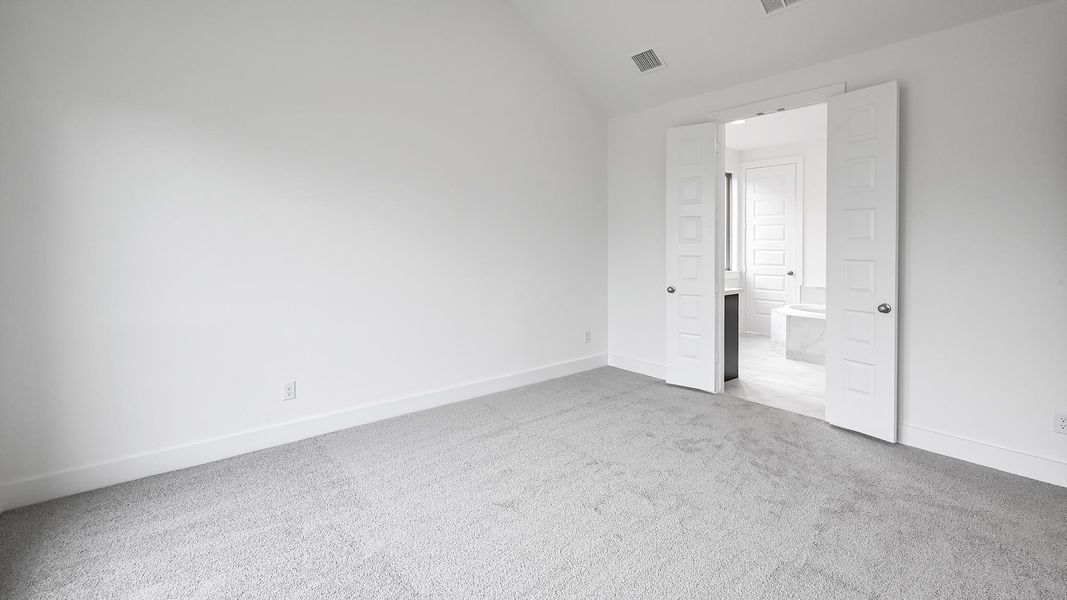 Unfurnished bedroom with baseboards, carpet flooring, ensuite bath, visible vents, and vaulted ceiling