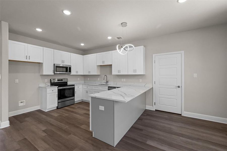 Kitchen featuring appliances with stainless steel finishes, kitchen peninsula, dark wood-type flooring, and light stone counters