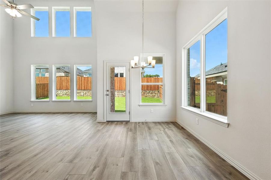 Unfurnished dining area featuring a chandelier, a towering ceiling, wood finished floors, and healthy amount of natural light Unfurnished dining area featuring a chandelier, a towering ceiling, wood finished floors, and healthy amount of natural light