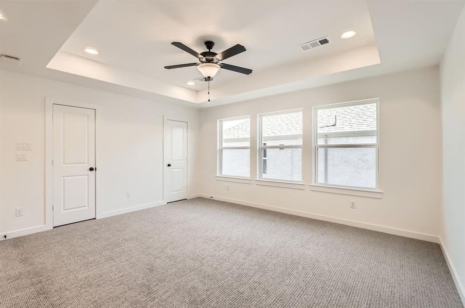 Carpeted spare room featuring ceiling fan and a raised ceiling