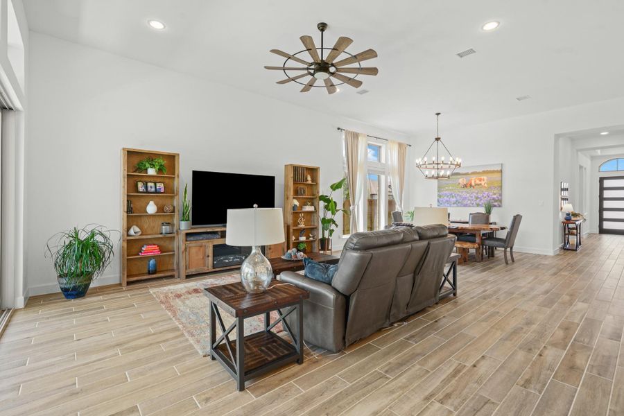 This spacious living area features an open floor plan with wood-look tile flooring.   Natural light floods in through large windows, and a modern chandelier highlights the adjoining dining space.
