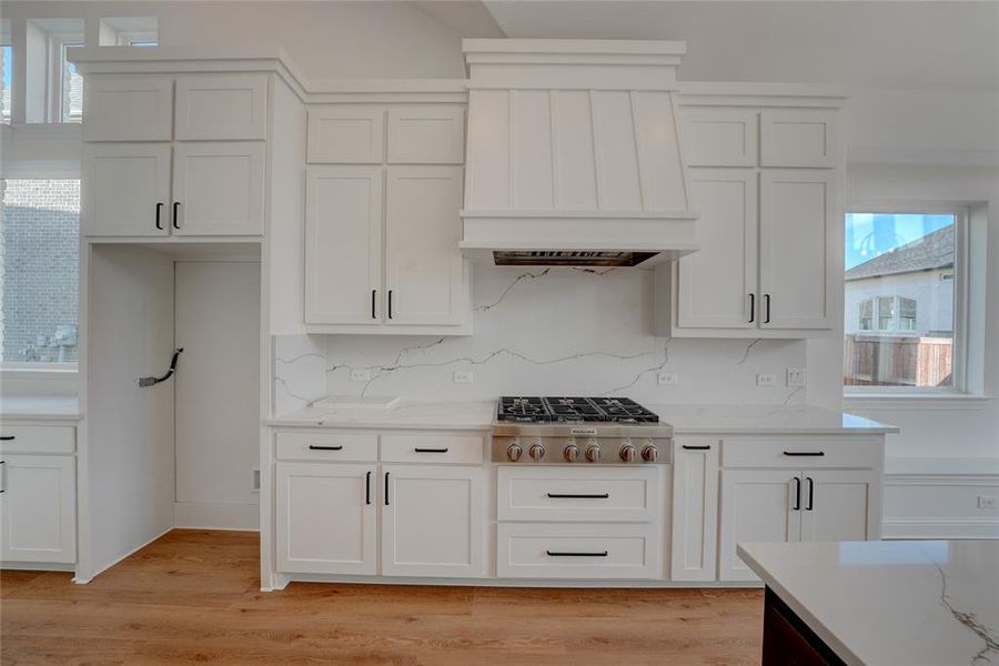 Kitchen with stainless steel gas cooktop, vinyl finished floors, custom range hood, backsplash, and white cabinetry