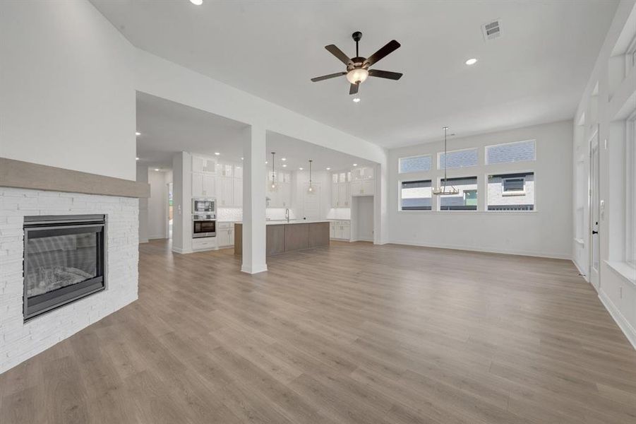 Spacious living area featuring light wood-finish flooring, a white brick fireplace with a substantial mantel, and a multi-paneled window array