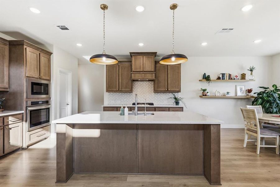 Kitchen featuring a large island with white countertop, wood-finish cabinetry, built-in stainless steel appliances, herringbone tile backsplash, and recessed lighting