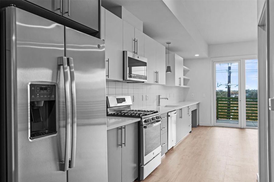 Kitchen featuring a sink, backsplash, light countertops, stainless steel appliances, and open shelves