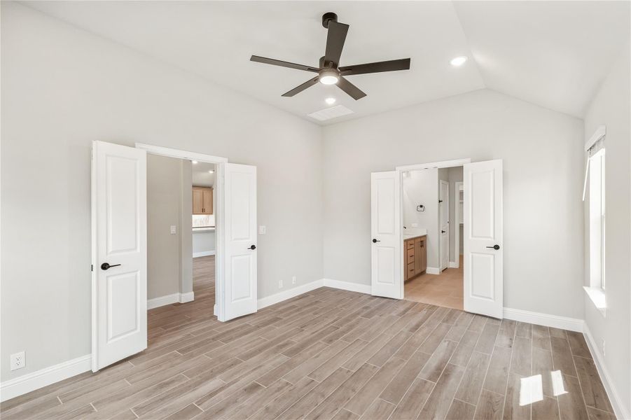 Empty bedroom with wood-look tile floors, ceiling fan, and doors leading to ensuite bathroom and closet