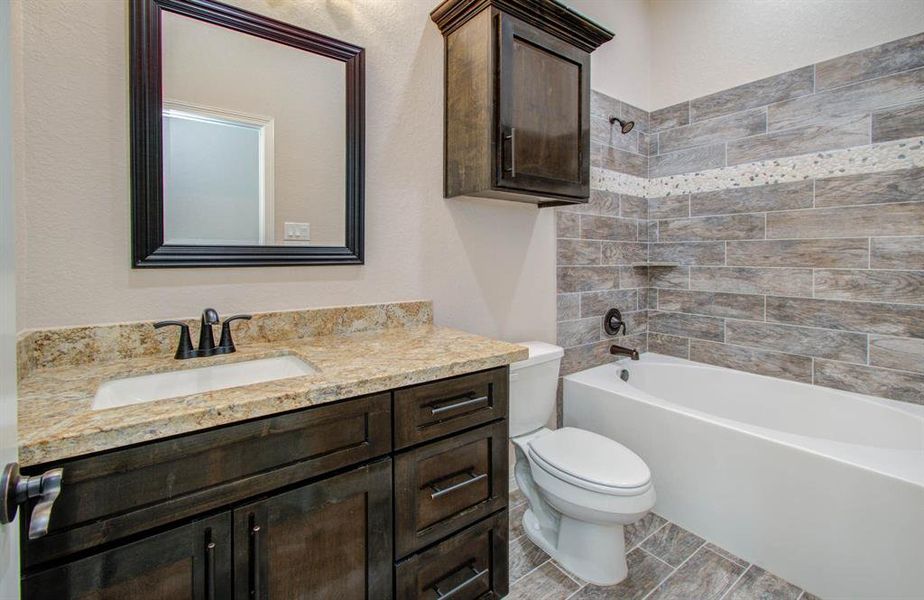 Modern bathroom featuring a dark wood vanity with granite countertop, undermount sink, large mirror, and a full bathtub with tiled surround.