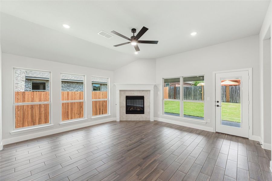 Open living room with tile fireplace, wood-look floors, ceiling fan, and large windows overlooking backyard Open living room with tile fireplace, wood-look floors, ceiling fan, and large windows overlooking backyard