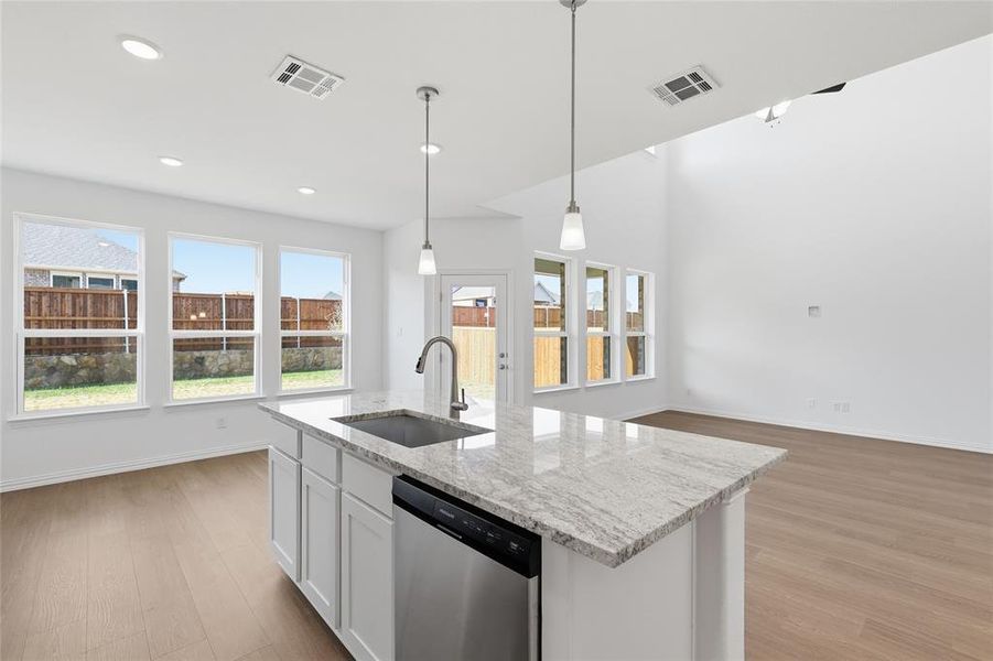 Kitchen featuring stainless steel dishwasher, white cabinetry, light stone countertops, a center island with sink, and light wood-type flooring