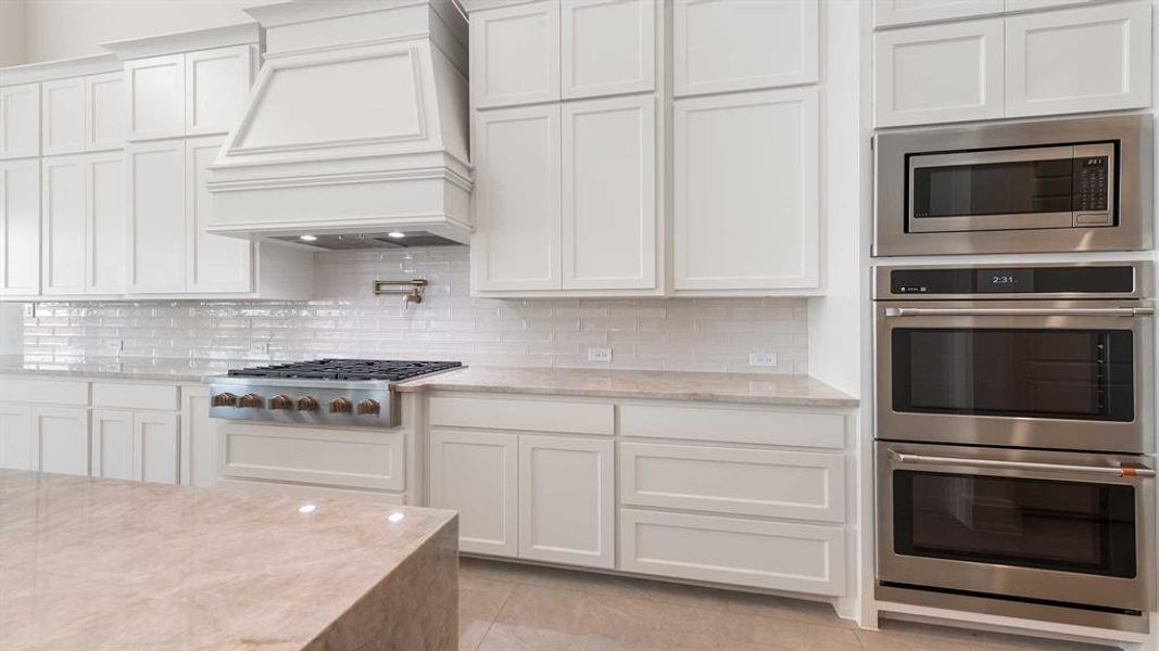 Kitchen featuring decorative backsplash, light stone countertops, white cabinetry, and stainless steel appliances