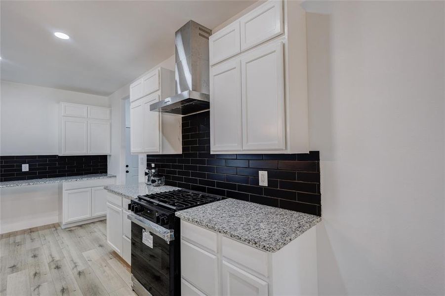 Kitchen with light wood-type flooring, wall chimney range hood, stainless steel gas range, and white cabinets