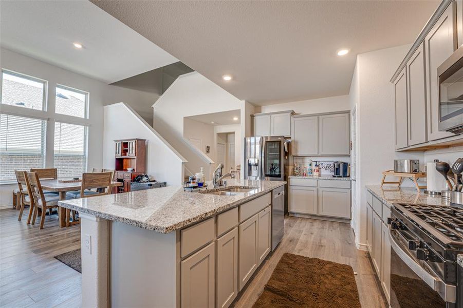 Kitchen with light wood finished floors, light stone counters, recessed lighting, an island with sink, and stainless steel appliances