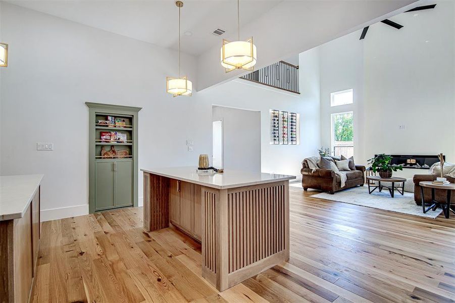 Kitchen with hanging light fixtures, light wood-style floors, a high ceiling, open floor plan, and light quartz counters and a double Island. Kitchen with hanging light fixtures, light wood-style floors, a high ceiling, open floor plan, and light quartz counters and a double Island.