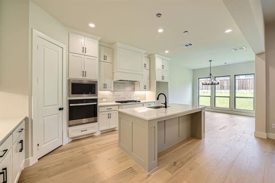 Kitchen with appliances with stainless steel finishes, tasteful backsplash, a chandelier, white cabinetry, and light wood-style floors Kitchen with appliances with stainless steel finishes, tasteful backsplash, a chandelier, white cabinetry, and light wood-style floors
