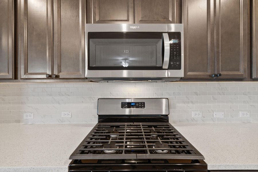Kitchen with range with gas cooktop, stainless steel microwave, dark brown cabinetry, light stone countertops, and decorative backsplash Kitchen with range with gas cooktop, stainless steel microwave, dark brown cabinetry, light stone countertops, and decorative backsplash