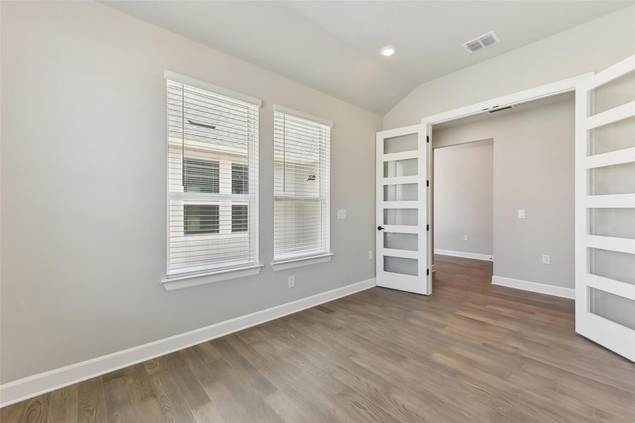 Empty room featuring wood finished floors, french doors, baseboards, and lofted ceiling Empty room featuring wood finished floors, french doors, baseboards, and lofted ceiling