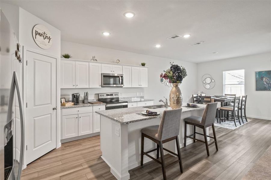 Kitchen featuring appliances with stainless steel finishes, a kitchen breakfast bar, a center island with sink, white cabinetry, and light stone counters