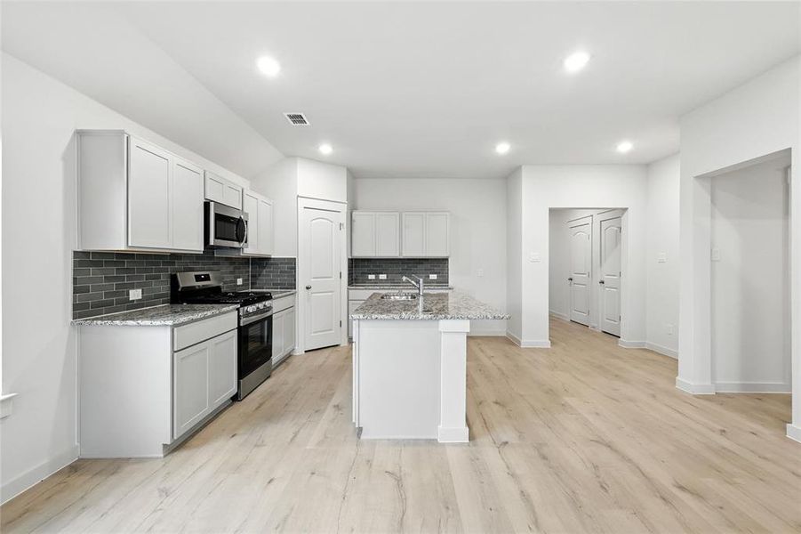 Kitchen featuring appliances with stainless steel finishes, tasteful backsplash, light stone countertops, a center island with sink, and recessed lighting