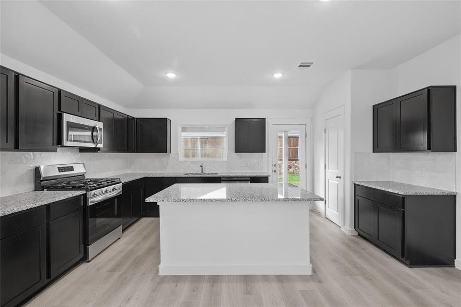 Kitchen featuring lofted ceiling, stainless steel appliances, decorative backsplash, a kitchen island, and light wood-style floors