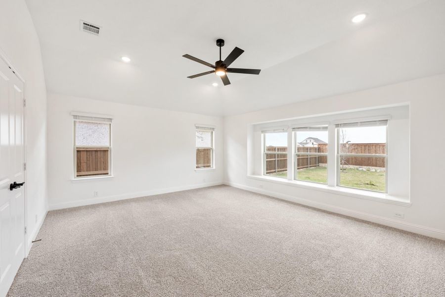 Spacious empty bedroom with carpet, ceiling fan, and large windows overlooking a fenced backyard
