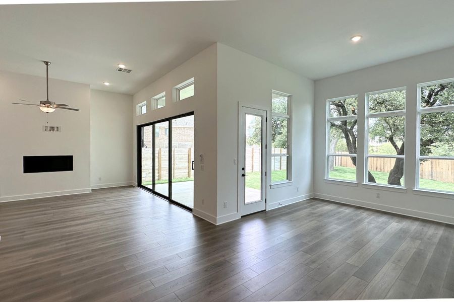 A spacious living area with abundant natural light, a modern fireplace, and large windows framing backyard trees.