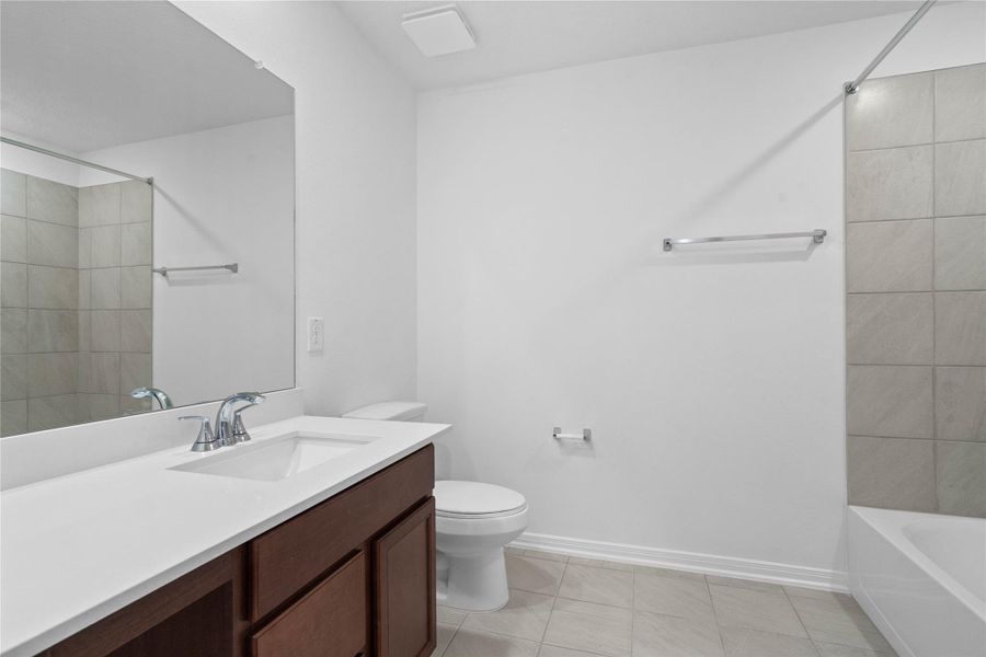 The secondary bathroom showcases tile flooring, a bath/shower combo with a Daltile tile surround, a vanity with knee space and a stunning light countertop, a mirror, sleek fixtures, and contemporary finishes throughout.