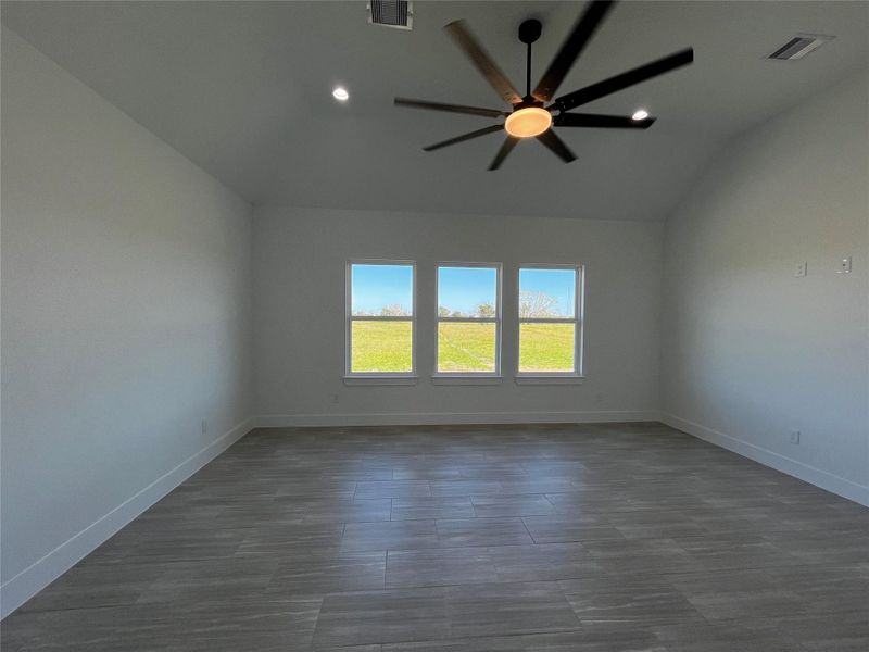 A spacious, modern room with large windows offering abundant natural light and a scenic outdoor view. The room features sleek flooring, white walls, and a stylish ceiling fan.