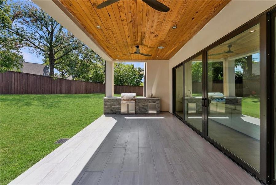 Fenced backyard featuring exterior kitchen, a patio, and a ceiling fan