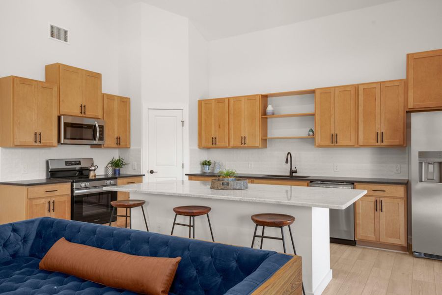 Kitchen with backsplash, stainless steel appliances, a towering ceiling, dark stone countertops, and light brown cabinetry