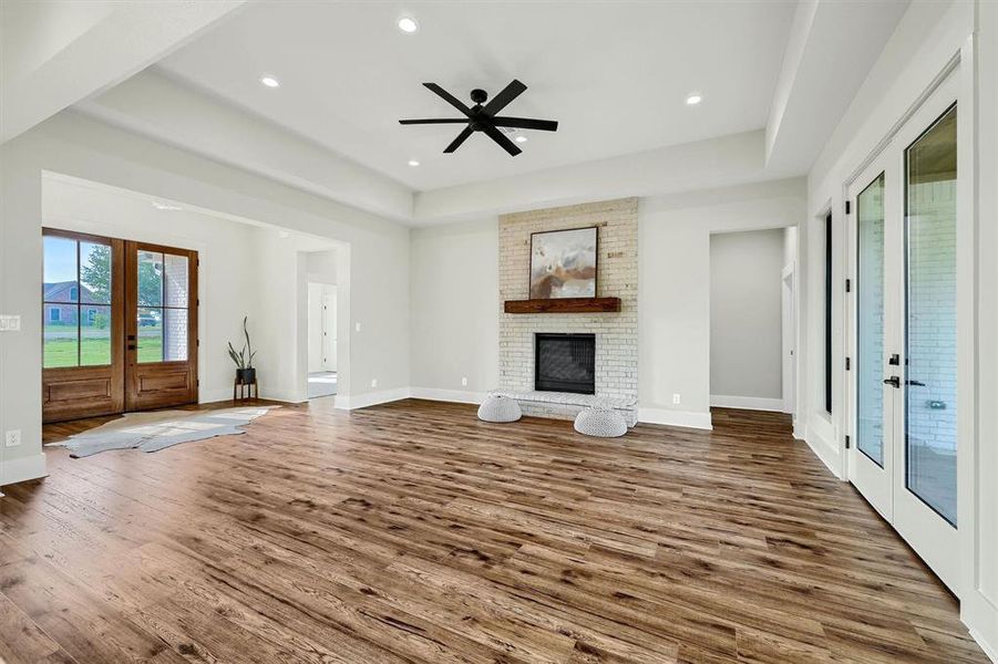 Unfurnished living room with ceiling fan, french doors, hardwood / wood-style flooring, a brick fireplace, and a tray ceiling