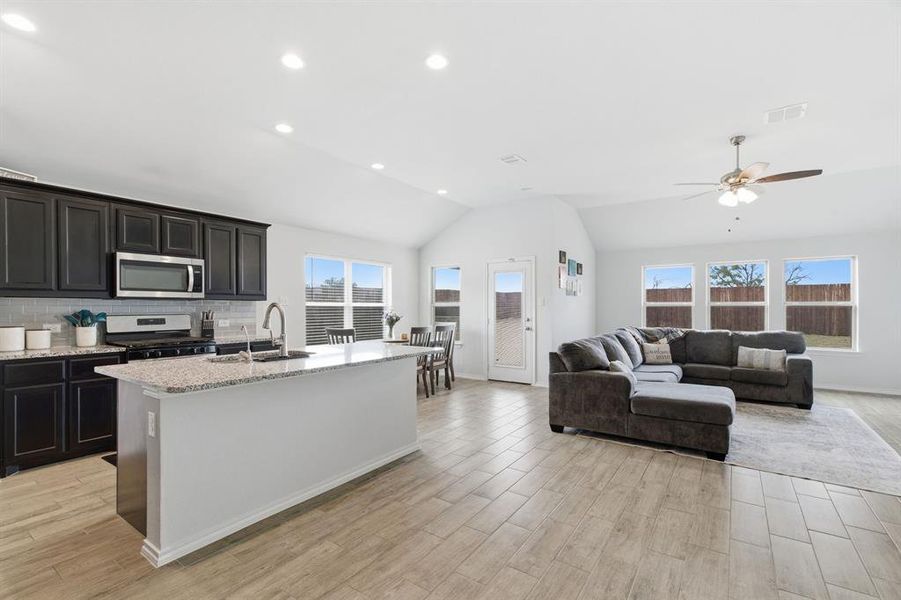 Kitchen featuring a kitchen island with sink, light stone countertops, vaulted ceiling, stainless steel appliances, and wood tiled floors