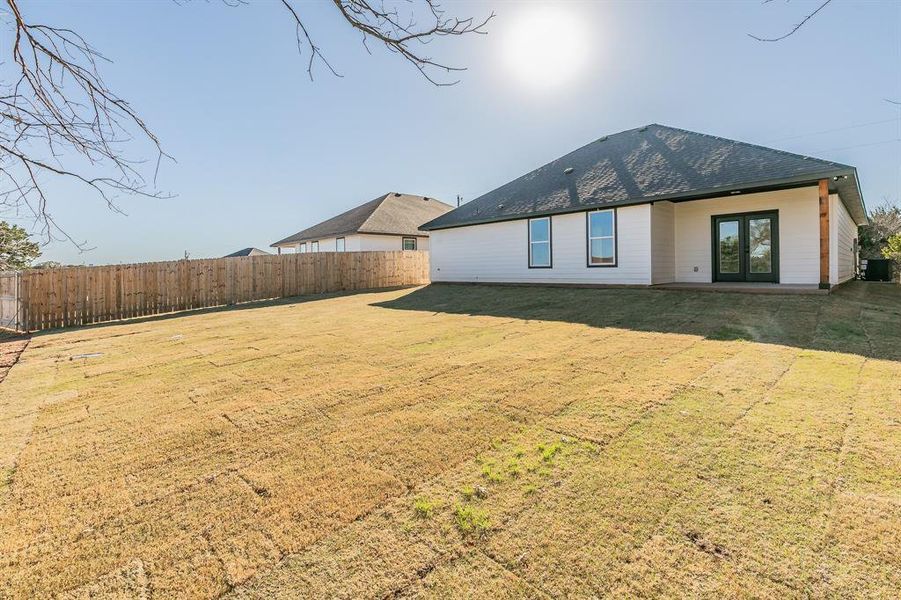 Rear view of property featuring a yard, roof with shingles, fence, and french doors