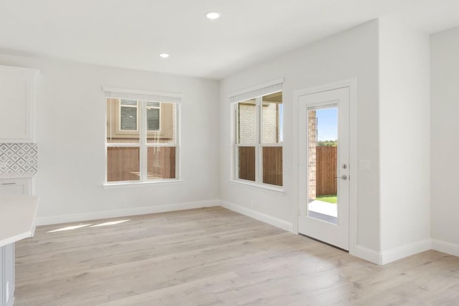 Bright empty room with light wood floors, white walls, two windows, and a glass back door