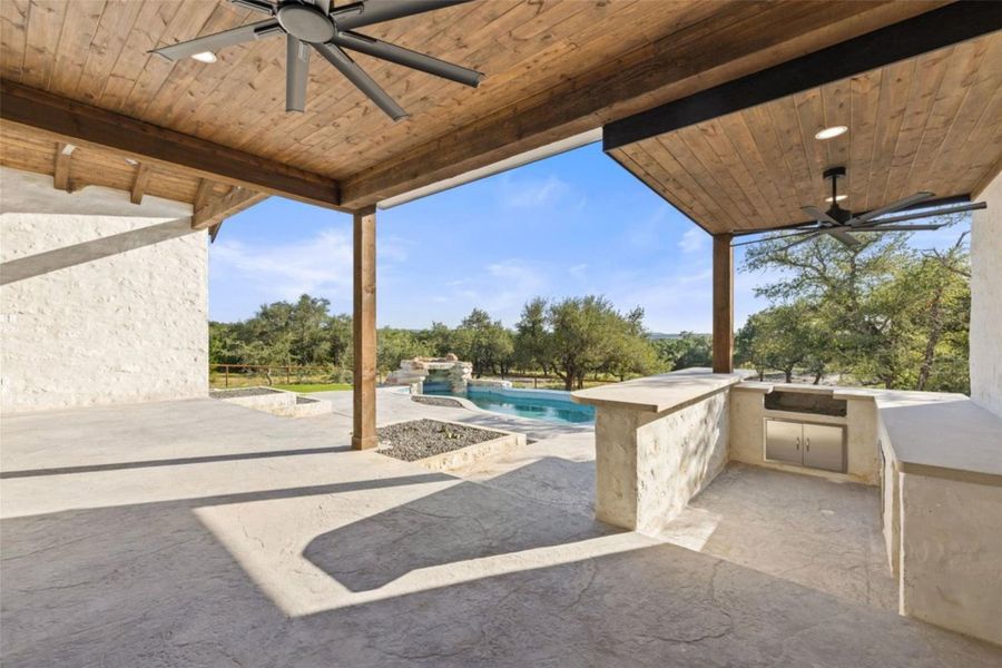 An inviting outdoor oasis features a covered patio with an outdoor kitchen, overlooking a pristine pool and serene landscape. An inviting outdoor oasis features a covered patio with an outdoor kitchen, overlooking a pristine pool and serene landscape.