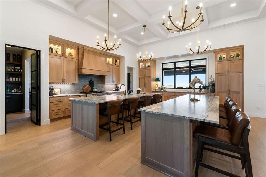 Kitchen with a kitchen bar, glass insert cabinets, light stone countertops, coffered ceiling, and premium range hood Kitchen with a kitchen bar, glass insert cabinets, light stone countertops, coffered ceiling, and premium range hood