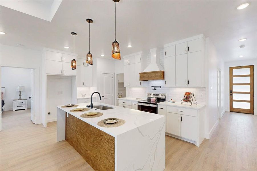 Kitchen with white cabinetry, a center island with sink, sink, stainless steel range with electric stovetop, and custom exhaust hood