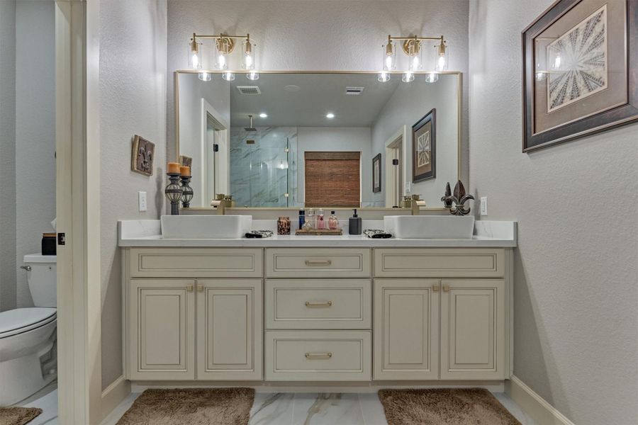 Elegant dual vanities with sleek quartz countertops, modern vessel sinks, custom cabinetry, and a large framed mirror illuminated by designer lighting. Elegant dual vanities with sleek quartz countertops, modern vessel sinks, custom cabinetry, and a large framed mirror illuminated by designer lighting.