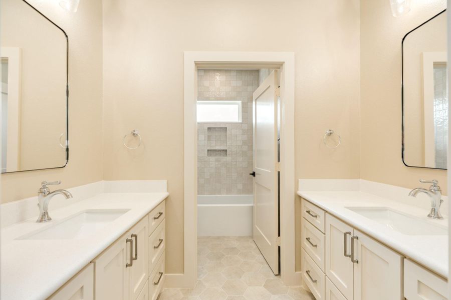 Bright bathroom with dual sinks and vanities, custom cabinetry, and a bathtub/shower combo. Neutral tones create a clean, inviting space. The tub is a deep tub perfect for soaking.